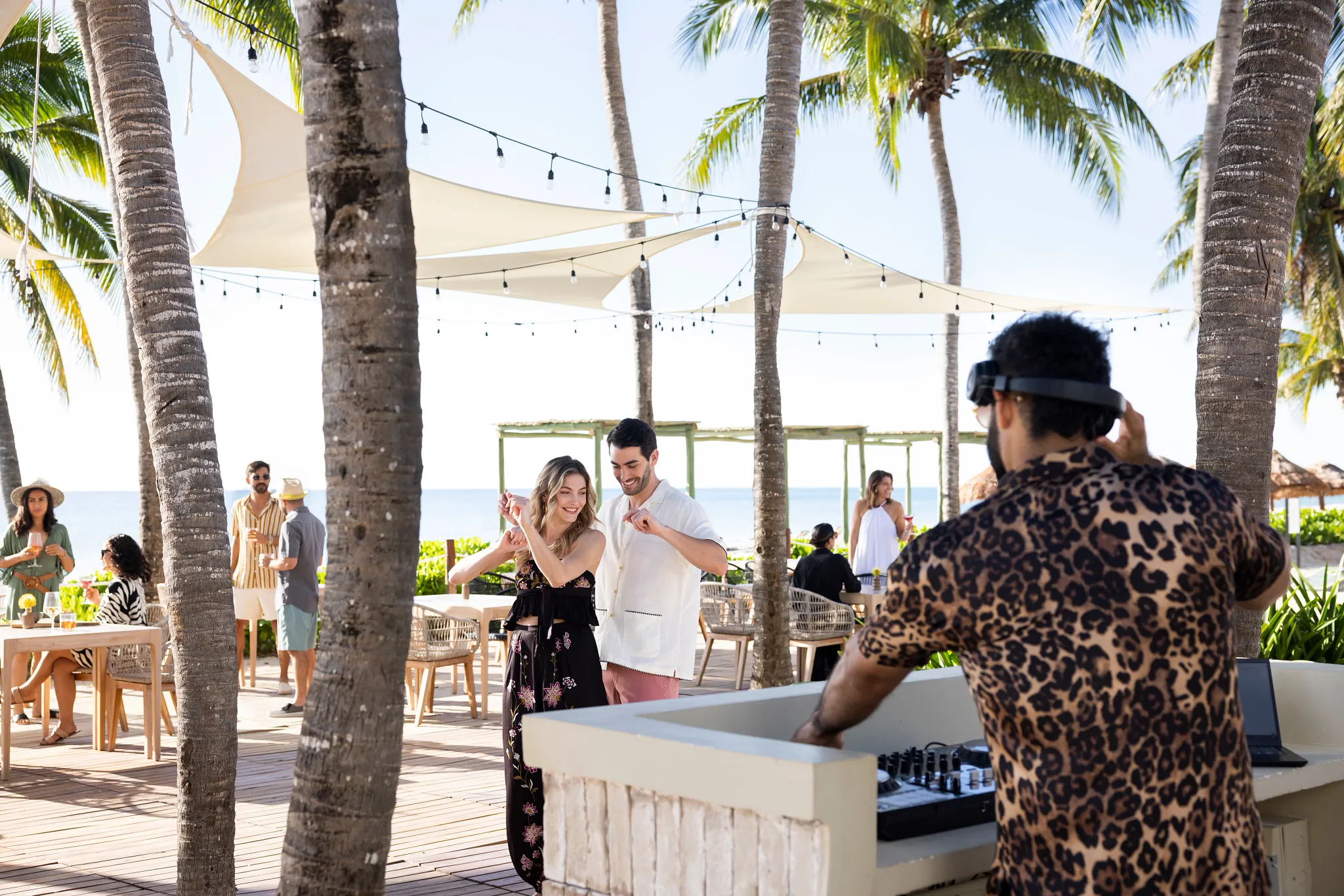 Guests dancing near a DJ booth at a beachfront lounge with palm trees at Hyatt Zilara Riviera Maya.