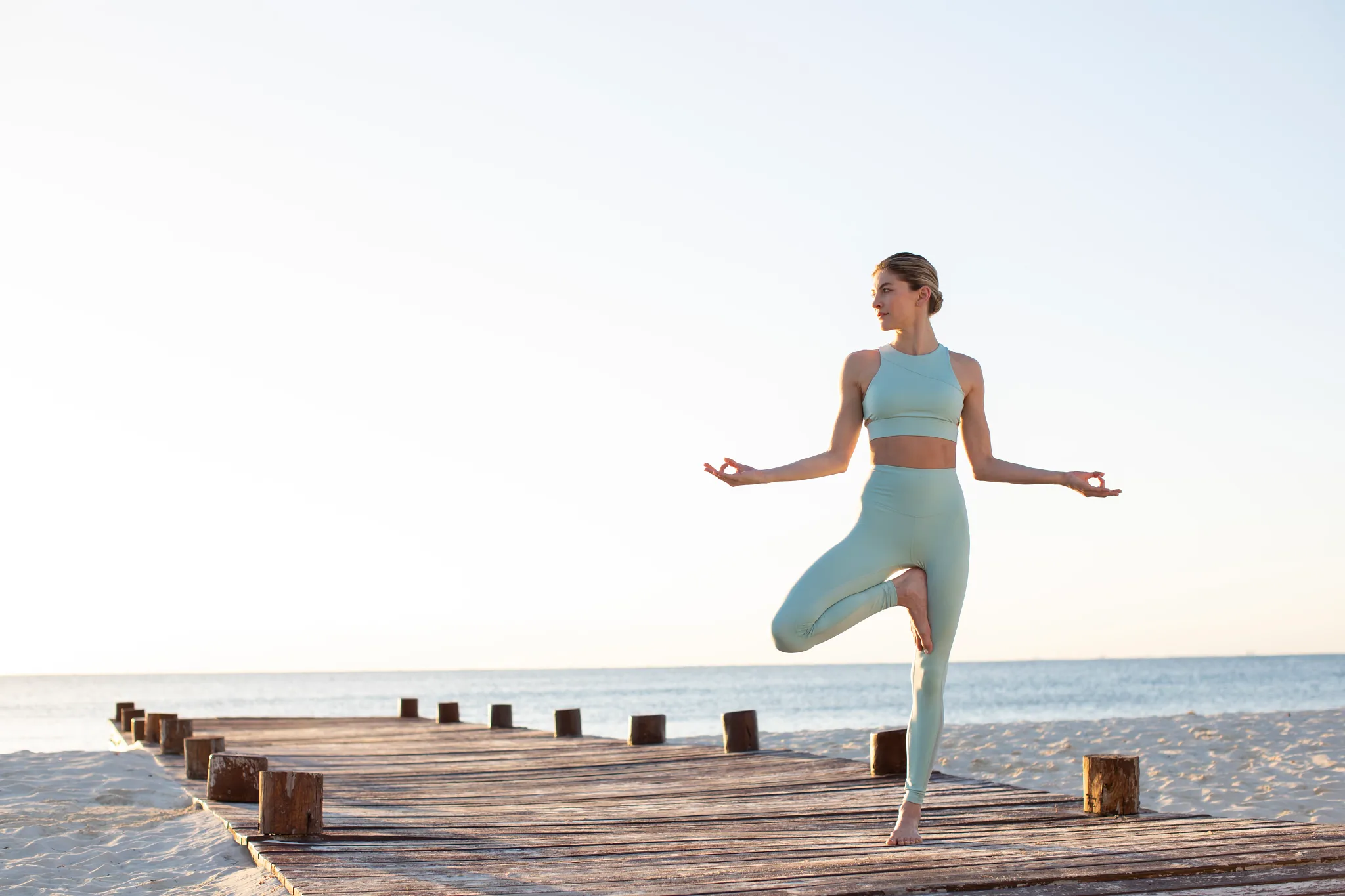Woman practicing yoga on a wooden deck by the beach at Hyatt Zilara Riviera Maya during sunrise, highlighting wellness experiences.