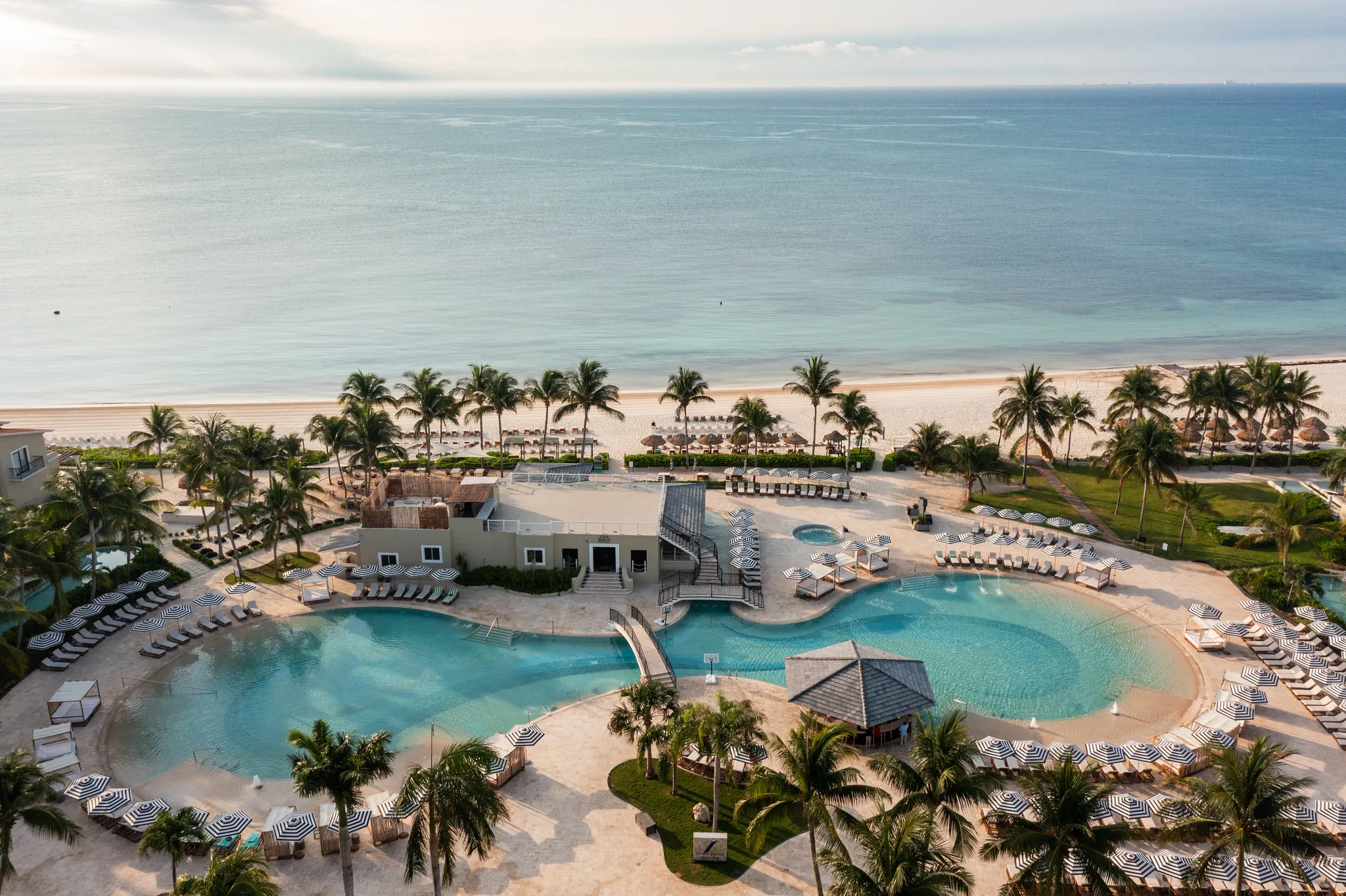 Lagoon-style pool overlooking the beach with lounge chairs and palm trees at Hyatt Zilara Riviera Maya.