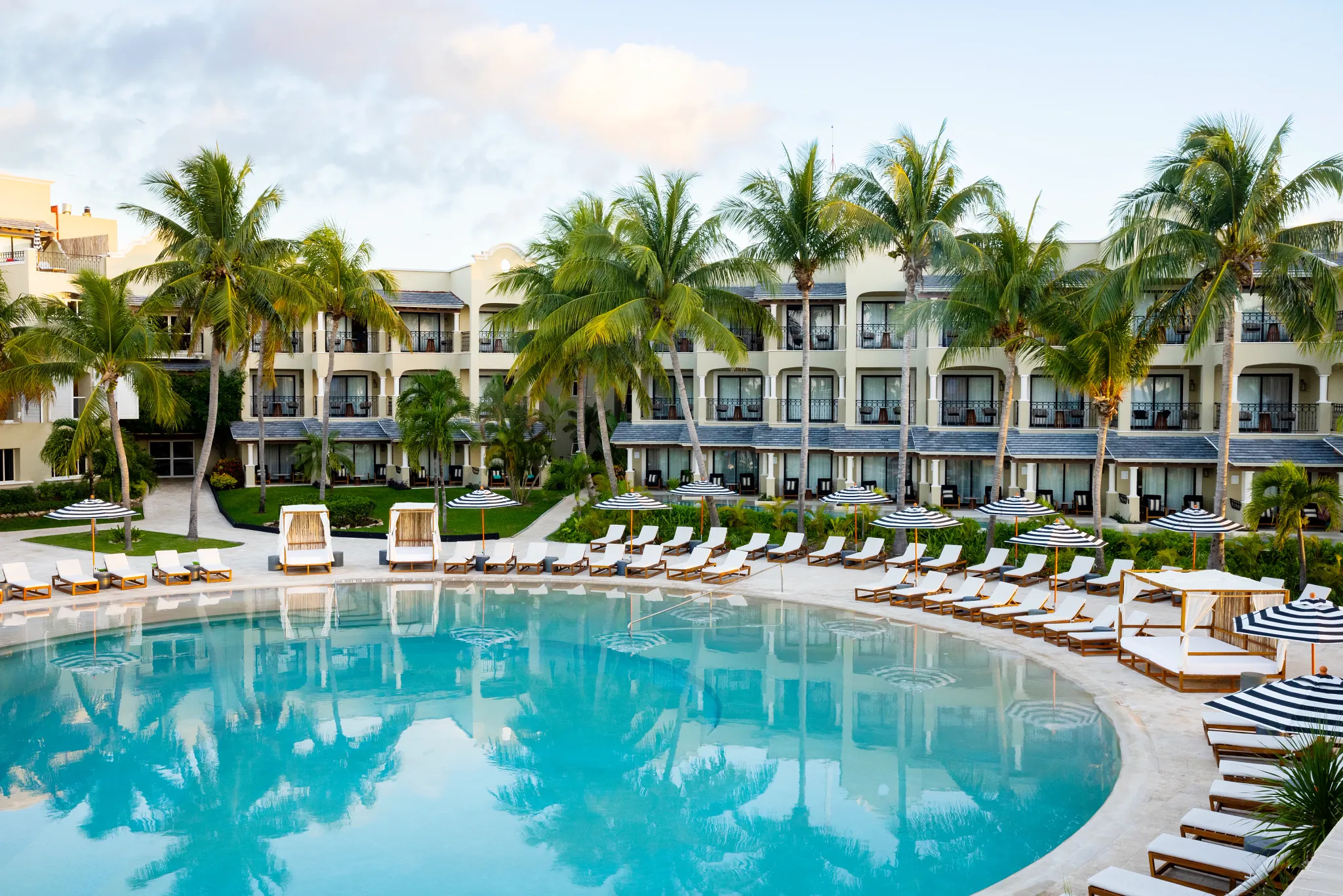 Expansive main pool surrounded by lounge chairs and palm trees at Hyatt Zilara Riviera Maya, offering a tranquil adults-only beachfront setting.