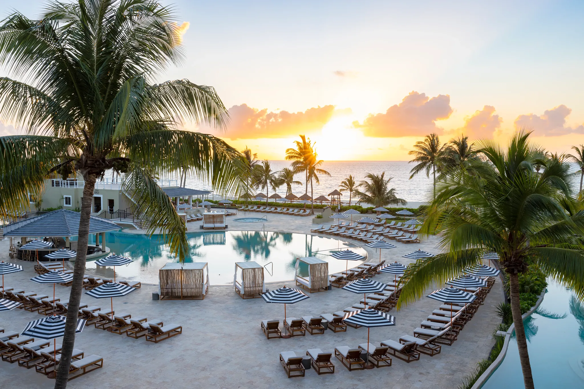Sunset view over the main pool and beachfront lined with palm trees and cabanas at Hyatt Zilara Riviera Maya.