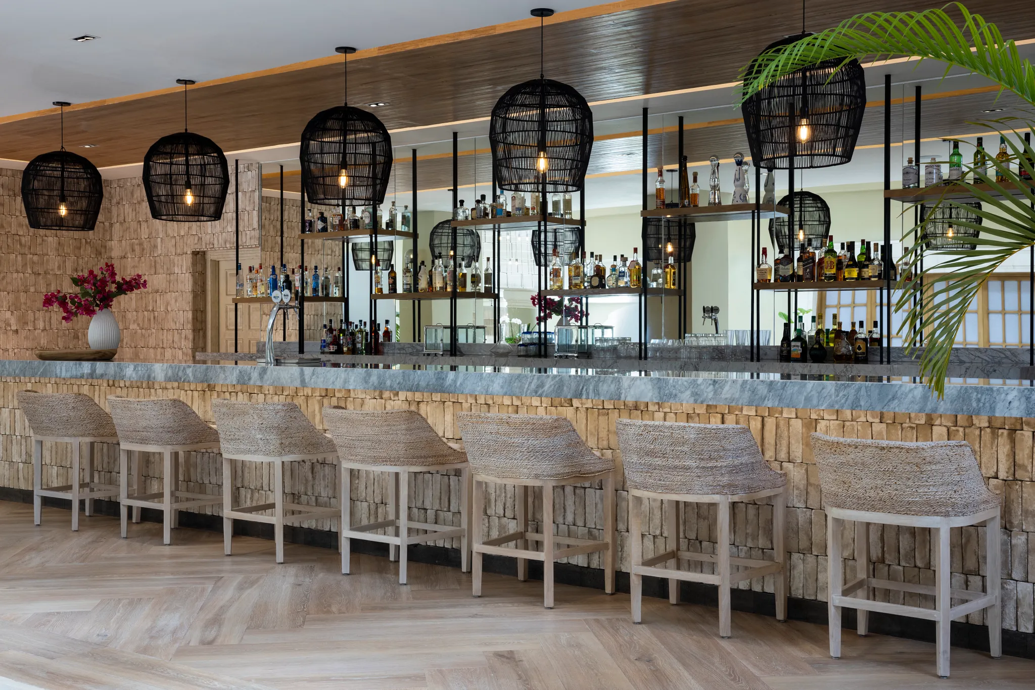 Social Lobby Bar at Hyatt Zilara Riviera Maya featuring a modern bar with woven seating, marble countertop, and stylish pendant lighting.